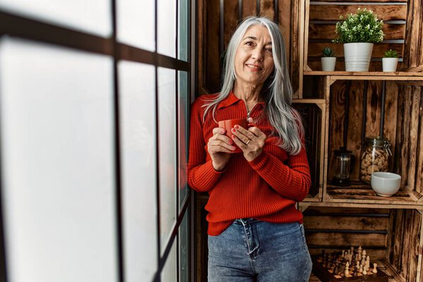 Middle age grey-haired woman smiling confident drinking coffee at home