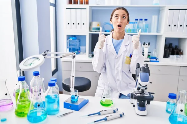 Young Brunette Woman Working Scientist Laboratory Amazed Surprised Looking Pointing — Fotografia de Stock