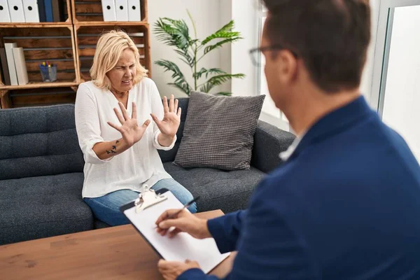 Middle age woman at psychology therapy office afraid and terrified with fear expression stop gesture with hands, shouting in shock. panic concept.