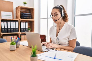 Ofiste çağrı merkezi kulaklığı takan Latin kökenli genç bir kadın korkmuş ve şaşırmış bir şekilde ağzı açık kalmış, inançsız bir yüz. 