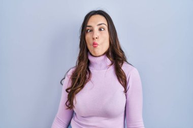 Mavi arka planda duran genç esmer kadın dudaklarıyla balık suratı yapıyor, çılgınca ve komik bir jest. Komik ifade. 