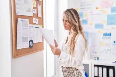 Genç sarışın iş kadını ofiste belge okuyor.