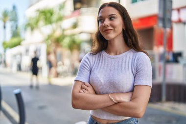 Kendine güvenen genç bir kadın caddede kollarını kavuşturmuş duruyor.