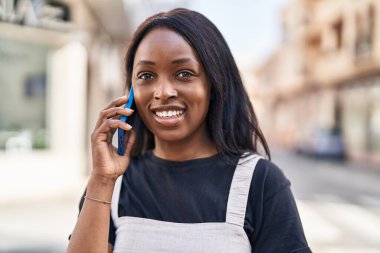 Genç Afrikalı Amerikalı kadın gülümsüyor. Kendine güveni tam. Sokakta akıllı telefondan konuşuyor.