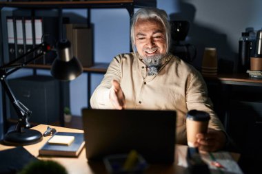 Gri saçlı, gece ofiste çalışan orta yaşlı bir adam dostça gülümseyerek selamlaşma ve hoş geldin diyor. başarılı iş. 