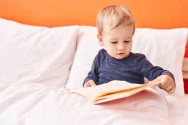 Sevimli sarışın çocuk yatak odasında oturmuş masal kitabı okuyor.
