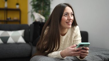 Evdeki kanepede uzanmış akıllı telefon kullanan genç, güzel İspanyol kadın.