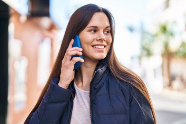 Genç, güzel, İspanyol bir kadın gülümsüyor ve caddede akıllı telefondan konuşuyor.