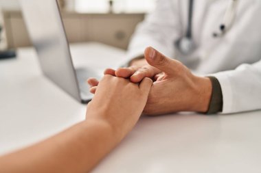 Man and woman doctor and patient having medical consultation with hands together at clinic