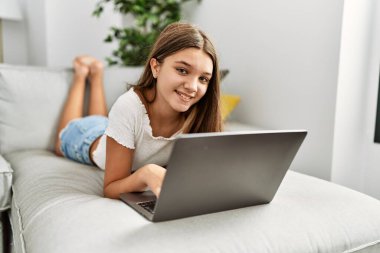 Evdeki kanepede dizüstü bilgisayar kullanan sevimli bir kız.