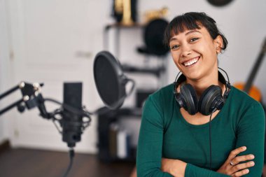 Güzel İspanyol kadın müzisyen gülümsüyor. Kollarını kavuşturup müzik stüdyosunda jest yapıyor.