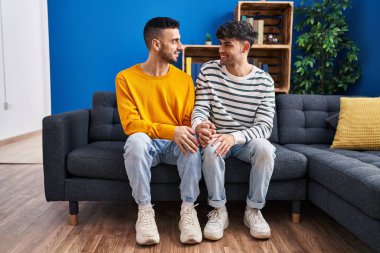 Kanepede oturan iki adam evde el ele oturuyorlar.