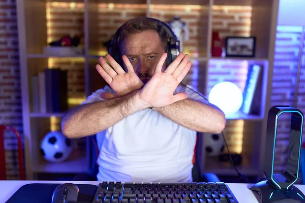 ひげを生やしている中世の男ビデオゲームをしているヘッドフォンの拒否式を身に着けている腕と手のひらを横断負の記号を行う 怒っている顔 — ストック写真