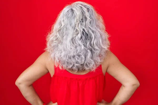 头发灰白的中年妇女站在红色的背景上 背向后看去 两臂交叉在身上 — 图库照片
