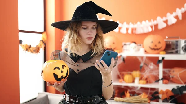 Young Blonde Woman Holding Halloween Pumpkin Basket Using Smartphone Home — Φωτογραφία Αρχείου