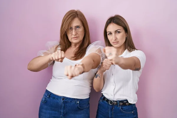 ヒスパニック系の母親と娘身に着けていますカジュアルホワイトTシャツ上のピンクの背景パンチング拳で戦います 積極的かつ怒っている攻撃 脅威と暴力 — ストック写真