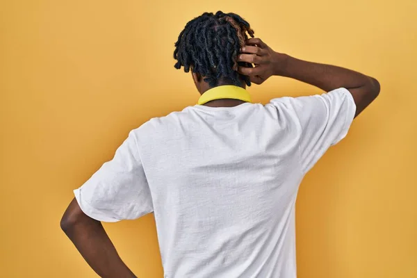 stock image Young african man with dreadlocks standing over yellow background backwards thinking about doubt with hand on head 