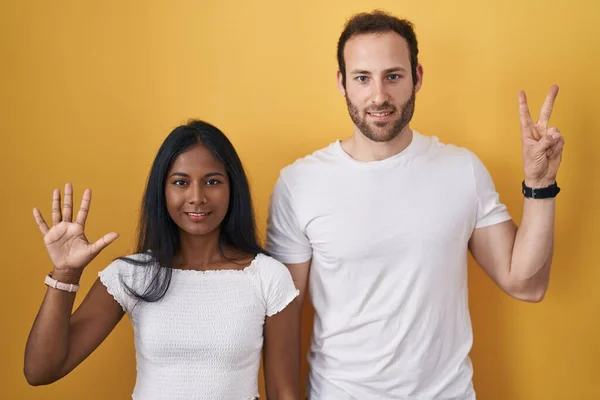 Interracial Couple Standing Yellow Background Showing Pointing Fingers Number Seven — Stock Photo, Image