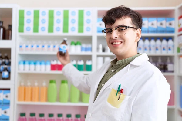 Non binary man pharmacist smiling confident holding medication bottle at pharmacy