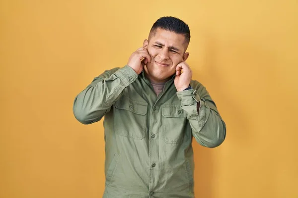 Латиноамериканец Стоит Жёлтом Фоне Закрывая Уши Пальцами Раздражённым Выражением Шума — стоковое фото