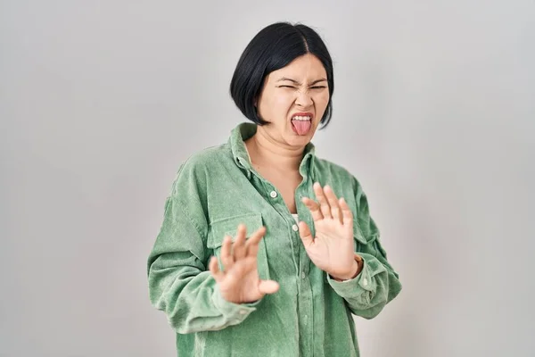 Young asian woman standing over white background disgusted expression, displeased and fearful doing disgust face because aversion reaction.