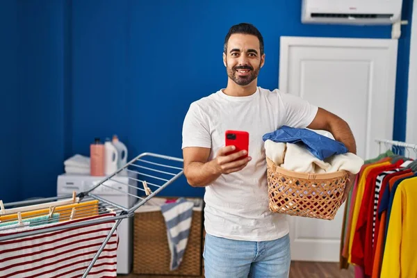 Young Hispanic Man Holding Basket Clothes Using Smartphone Laundry Room — Fotografia de Stock