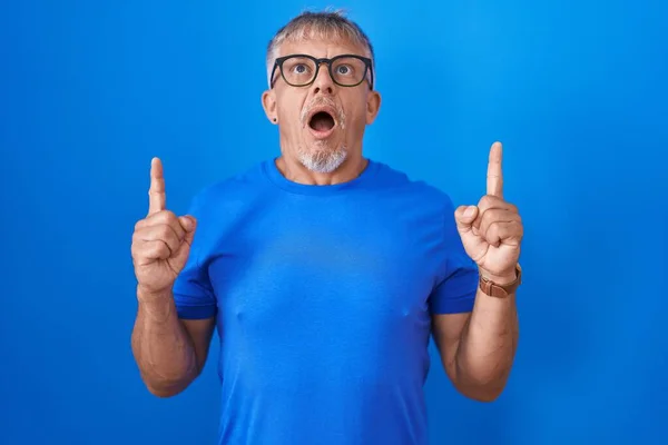 Hispanic Man Grey Hair Standing Blue Background Amazed Surprised Looking — Stock Photo, Image