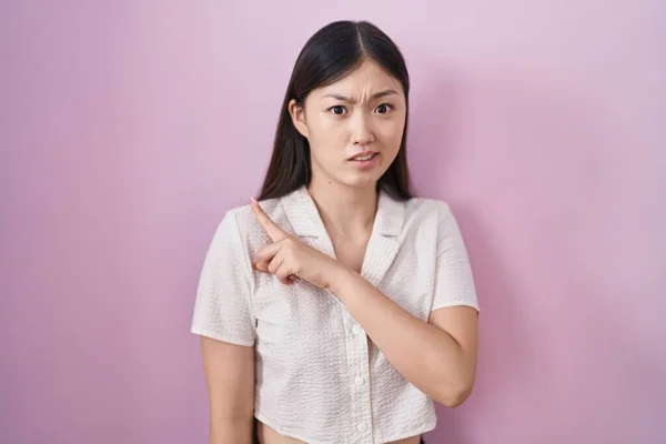 中国年轻女子站在粉红的背景上 用食指 关心和惊讶的表情将忧虑和紧张抛在一边 — 图库照片