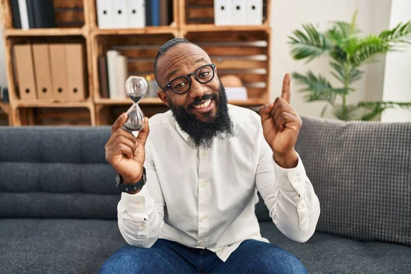 Hombre Afroamericano Sosteniendo Reloj Arena Oficina Sonriendo Feliz Señalando Con —  Fotos de Stock