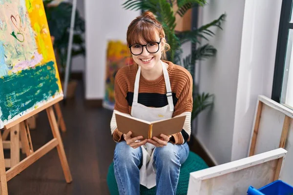 Νεαρή Γυναίκα Καλλιτέχνης Χαμογελά Αυτοπεποίθηση Βιβλίο Ανάγνωσης Στο Στούντιο Τέχνης — Φωτογραφία Αρχείου