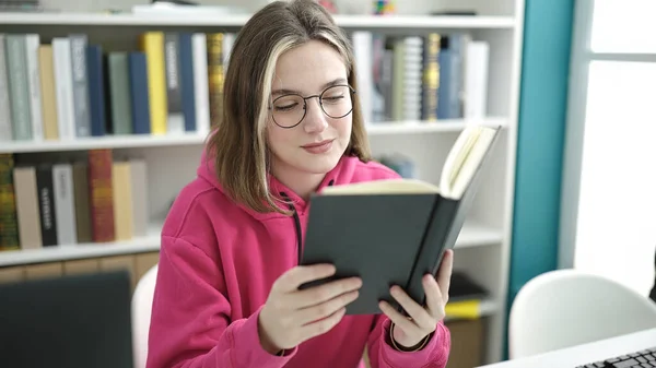 在图书馆大学 年轻的金发女学生坐在桌子上看书 — 图库照片