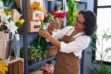 Genç ve güzel İspanyol çiçekçi çiçekçi çiçekçide çiçekçide akıllı telefonla fotoğraf çekiyor.