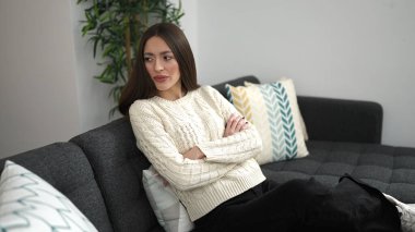 Young beautiful hispanic woman sitting on sofa with serious expression at home