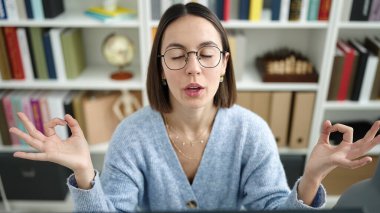 Young beautiful hispanic woman student doing yoga exercise at library university