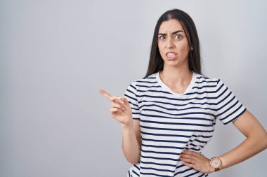 Çizgili tişört giyen genç esmer kadın endişeli, endişeli ve şaşırmış bir ifade takınıyor. 