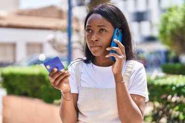 Genç Afro-Amerikalı kadın akıllı telefondan konuşuyor ve park yerinde kredi kartı kullanıyor.