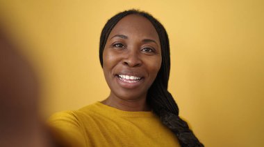 African woman taking selfie smiling over isolated yellow background