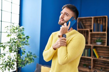 Genç İspanyol adam evde endişeli bir ifadeyle akıllı telefondan konuşuyor.