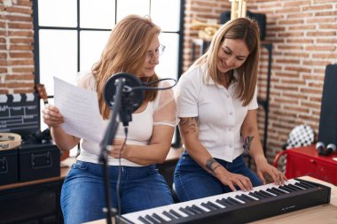 Mother and daughter musicians singing song playing piano at music studio