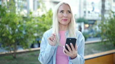 Parkta akıllı telefon kullanan, kendine güvenen genç sarışın kadın.