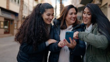 Mother and daugthers using smartphone standing together at street