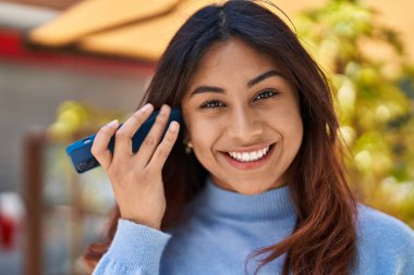 Young hispanic woman smiling confident listening audio message by the smartphone at street