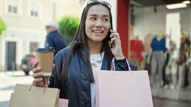 Güzel İspanyol bir kadın akıllı telefondan konuşuyor. Elinde alışveriş poşetleri ve sokakta kahve var.