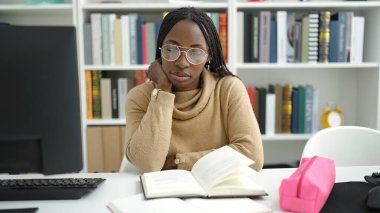 African woman reading a book sitting on desk at library university