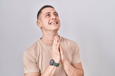 Young man standing over isolated background begging and praying with hands together with hope expression on face very emotional and worried. begging. 