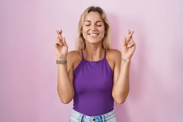 Young Blonde Woman Standing Pink Background Gesturing Finger Crossed Smiling — Foto de Stock