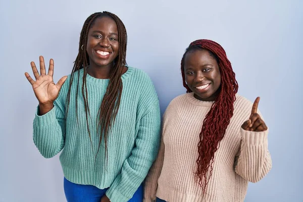 Две Африканки Стоят Синем Фоне Показывают Пальцем Номер Шесть Улыбаясь — стоковое фото