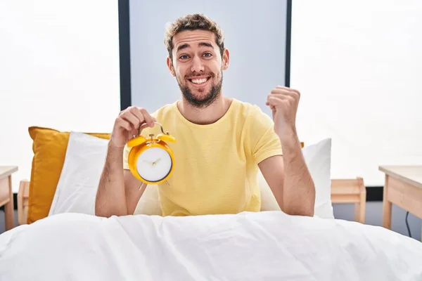 Homem Hispânico Com Barba Segurando Despertador Cama Gritando Orgulhoso Celebrando — Fotografia de Stock