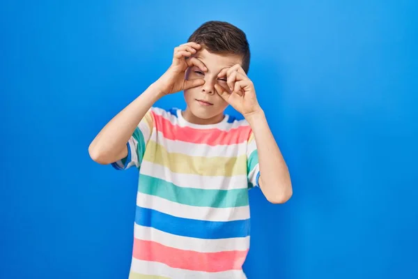 Genç Beyaz Çocuk Mavi Arka Planda Duruyor Parmaklarıyla Gözlerini Açmaya — Stok fotoğraf