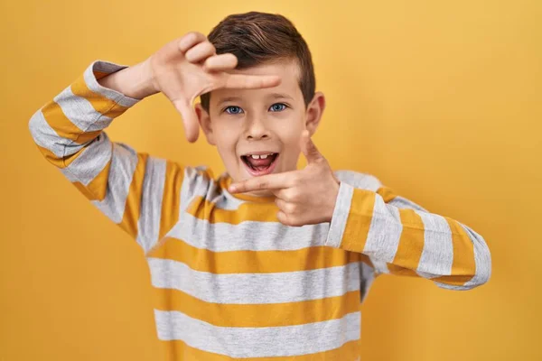 黄色の背景に立っている若い白人の子供は 幸せな顔をした手と指でフレームを作り笑顔 創造性と写真の概念 — ストック写真